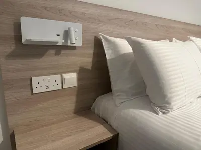 a bed with white pillows and a lightswitch on a wall at Melia Suites in Limassol