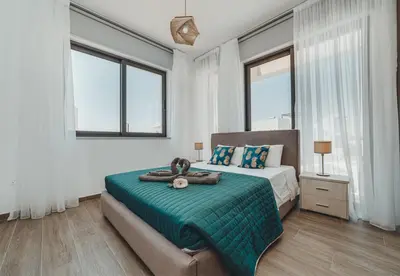 a bedroom with a bed with a green blanket and windows at STAY Villa Palm in Protaras