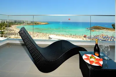 a table with a bottle of wine and a chair with a view at Vassos Nissi Plage Hotel & Spa in Ayia Napa