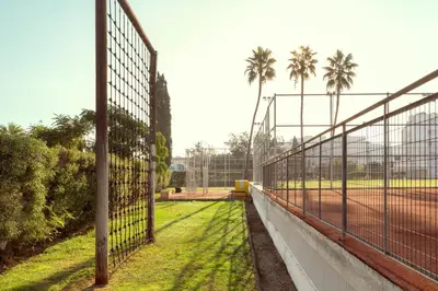 a tennis court with a fence and palm trees at SUNWING Sandy Bay Beach Village in Ayia Napa