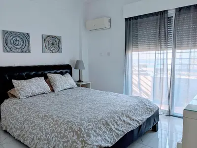 a white bedroom with a bed and a large window at Diana Apartment in Limassol