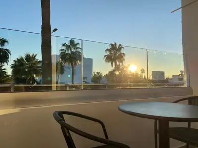 a table and chair on a balcony with a view of the sunset at Nissi Avenue Studios in Ayia Napa