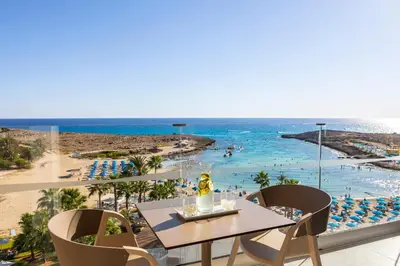 a balcony with a table and chairs and a beach at The HEALTHY Stay-Padel, Pool&Fitness in Ayia Napa