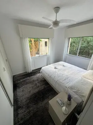a bedroom with a bed and a table and two windows at Georges 2 Bedroom Apartment in Limassol