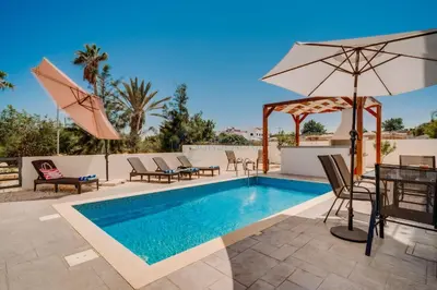 a swimming pool with a table and chairs and an umbrella at Alasia 16 - Modern smart villa in tranquil serenity in Paralimni