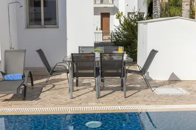 a dining table and chairs next to a swimming pool at Villa Palms 32 in Protaras