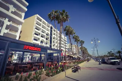 a city street with a restaurant and palm trees at Krasas Beach Apartment Rentals in Larnaka