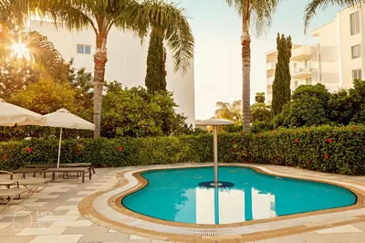 a swimming pool with palm trees and a building at Anesis Hotel in Ayia Napa