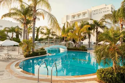a large swimming pool with palm trees in front of a hotel at Anesis Hotel in Ayia Napa
