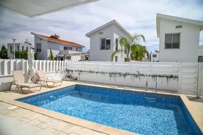 a swimming pool with two chairs next to a white fence at Hi royal villa in Pervolia