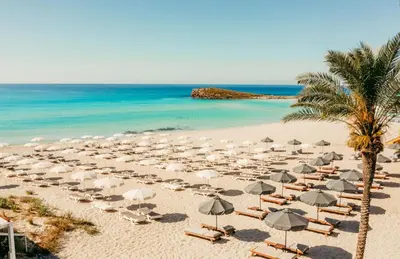 a beach with chairs and umbrellas and the ocean at Nissi Si Lux Boho Apartment on Nissi beach in Ayia Napa