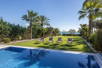 a swimming pool with two lawn chairs and palm trees at Ayia Napa Seafront Ionion Villa H5 in Ayia Napa