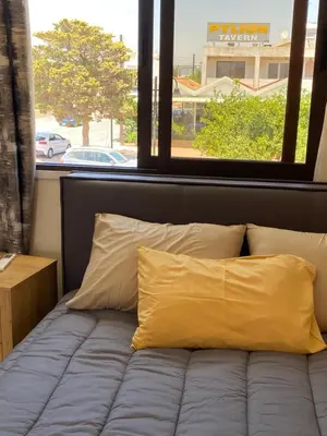 a bed with two yellow pillows in front of a window at A sea breeze house in Voroklini