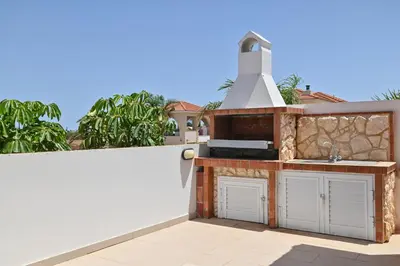 a backyard kitchen with a sink and a fence at Wealthystays 3BR Terrace BBQ Villa with pool in Liopetri