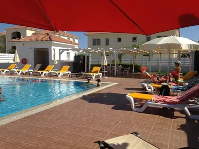 a pool with chairs and umbrellas and people sitting on them at Mythical Sands Resort - Africa in Protaras