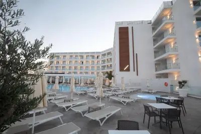 a hotel patio with tables and chairs and a pool at Evalena Beach Hotel in Protaras