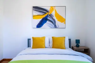 a bedroom with a bed with yellow pillows and a painting at Vibe - 1 Bedroom Apartment W Balcony in Larnaca in Larnaka
