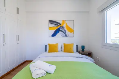 a white bedroom with a green bed with yellow pillows at Vibe - 1 Bedroom Apartment W Balcony in Larnaca in Larnaka
