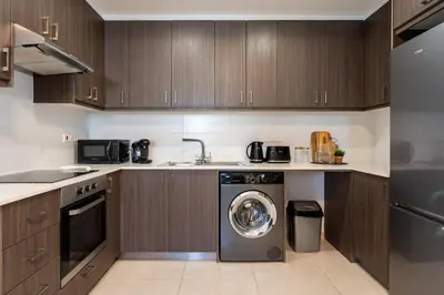 a kitchen with wooden cabinets and a washing machine at Valleria - 2 BR Apartment W Pool in Larnaca in Larnaka