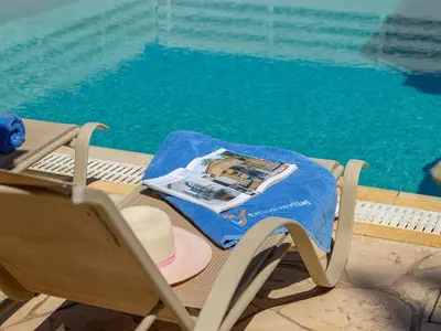 a chair with a hat and a magazine next to a pool at villa Sama palms 21 in Protaras