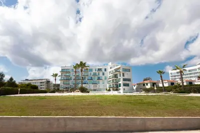 a large white building with palm trees in front of it at Apartment Marisol - Beachfront in Protaras