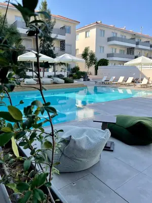 a swimming pool with chairs and umbrellas next to a building at Mythical Sands Resort, Protaras, Choose Joy Apt in Paralimni