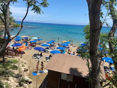 a beach with a lot of people with blue umbrellas at Ionian Breeze Family House Walk to Beach And Dining in Paralimni