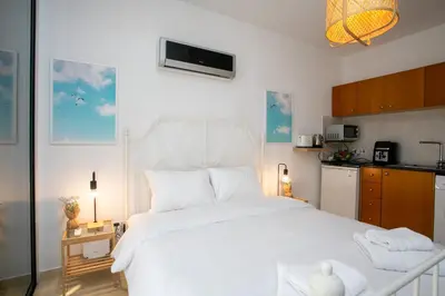 a bedroom with a large white bed and a kitchen at Palmove Makenzy Ria Studio in Larnaka