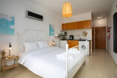 a bedroom with a white bed and a kitchen at Palmove Makenzy Ria Studio in Larnaka