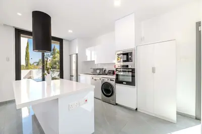 a kitchen with white cabinets and a washer and dryer at By The Beach - Aura Villa in Protaras