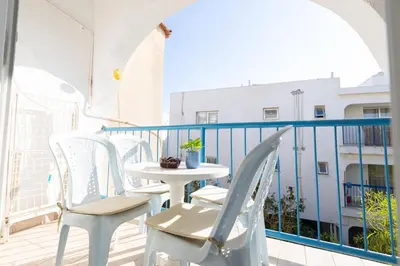a balcony with white chairs and a table and a building at Downtown apartment - Ayia Napa in Ayia Napa