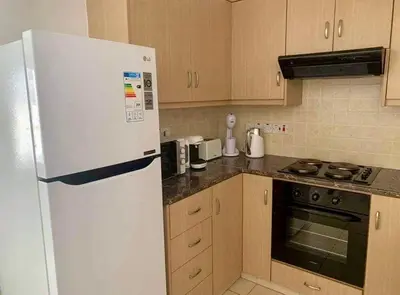 a kitchen with a white refrigerator and wooden cabinets at Beautiful 2 Bed Ground Floor Apartment With Pool in Paralimni