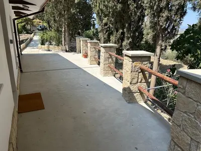 a concrete walkway with a stone fence and trees at Monolithos Cottage in Pachna