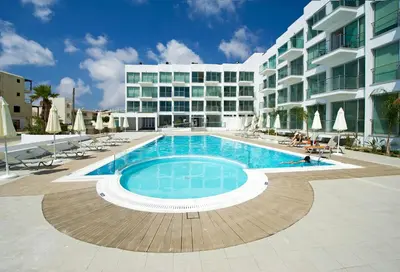 a swimming pool in front of a large building at Too Coool Studio Apartment Coralli Resort in Protaras