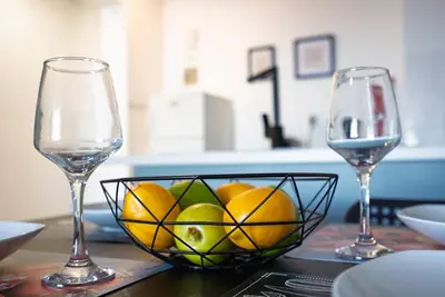 a bowl of fruit on a table with two wine glasses at Anteia's Seaview Suite just steps from Finikoudes Beach Larnaca in Larnaka