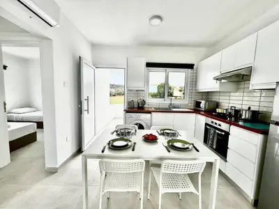 a white kitchen with a white table and chairs at Protaras Cozy2bedroom Apartment in Paralimni