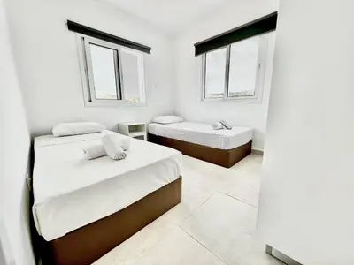two beds in a white room with two windows at Protaras Cozy2bedroom Apartment in Paralimni