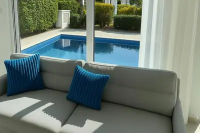 a couch with two blue pillows sitting in front of a window at Too Coool Villa Milos Lifestyle in Protaras