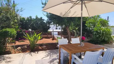 a wooden table with white chairs and an umbrella at HANA Holiday house in Ayia Napa