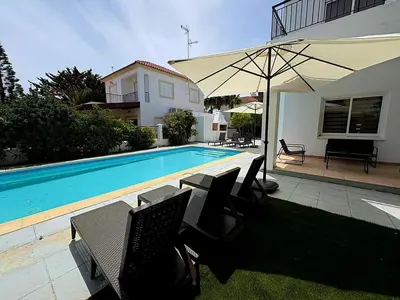 a pool with chairs and an umbrella next to a house at Villa Solmare in Pervolia