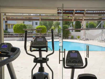 a gym with two exercise bikes in front of a swimming pool at Mediterranean Escape - Coastal 2-Bedroom Apartment Limassol in Limassol