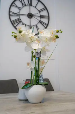 a vase with white flowers on a table with a clock at Seaview Suite49 steps to Mackenzie Beach Larnaca in Larnaka