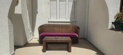 a wicker chair with a stool in front of a window at Sea Breeze Maisonette in Larnaka
