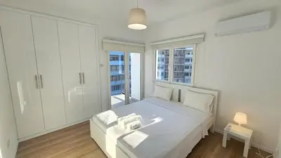 a white bedroom with a bed and a window at Kanika 3 bedroom city beach in Limassol