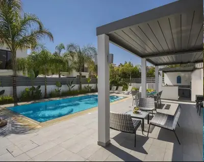 a patio with a table and chairs and a swimming pool at Sandy Feet Beach House in Paralimni