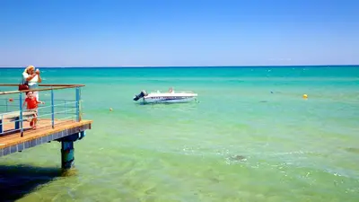 a woman standing on a pier with a boat in the water at Modern Larnaca Beach Apartment in Larnaka