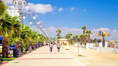 two people walking down a sidewalk with palm trees at Modern Larnaca Beach Apartment in Larnaka