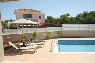 a pool with chairs and an umbrella next to a house at Mimosa 18 Beachhouse Villa in Protaras
