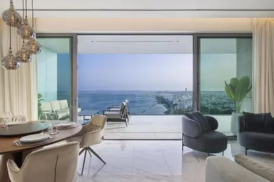 a living room with a table and chairs and a large window at Trilogy Limassol Seafront in Limassol