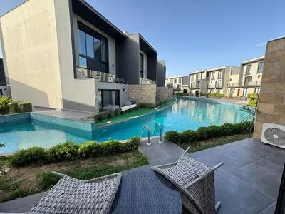 a swimming pool with two chairs next to a building at Kervansaray Comfort in Ayii Trimithias